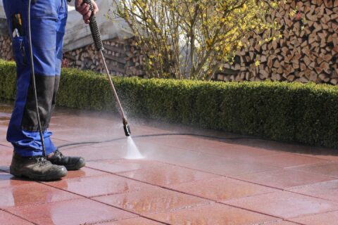 Image of man in jeans pressure washing outdoor tile floor